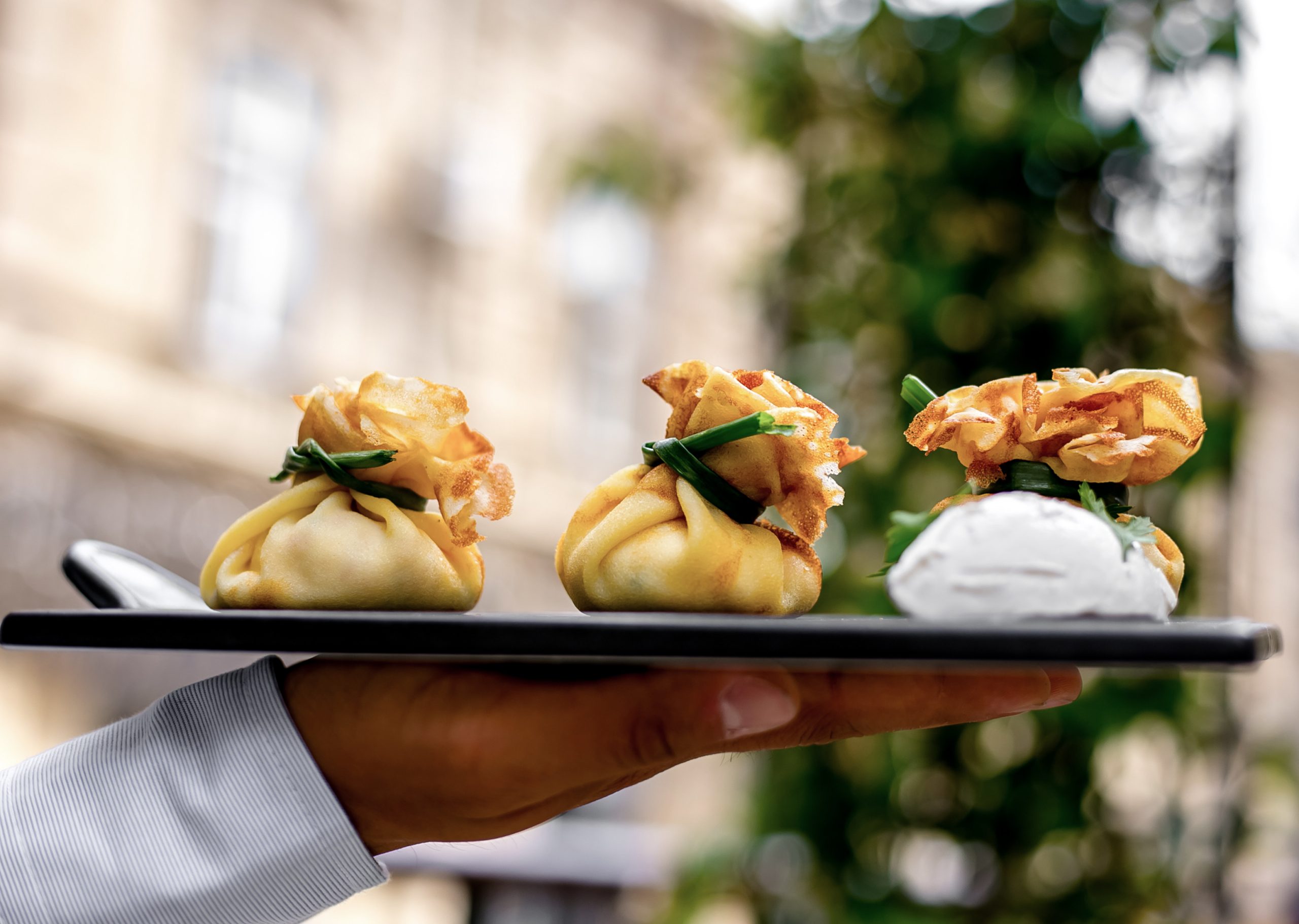 front view a man holds a tray with khinkali pancakes with sour cream and herbs